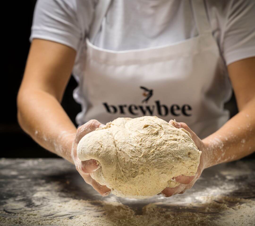 Person formt einen frischen Pizzateig auf bemehlter Arbeitsfläche, Nahaufnahme aus der Küche – zeigt handwerkliche Teigzubereitung.