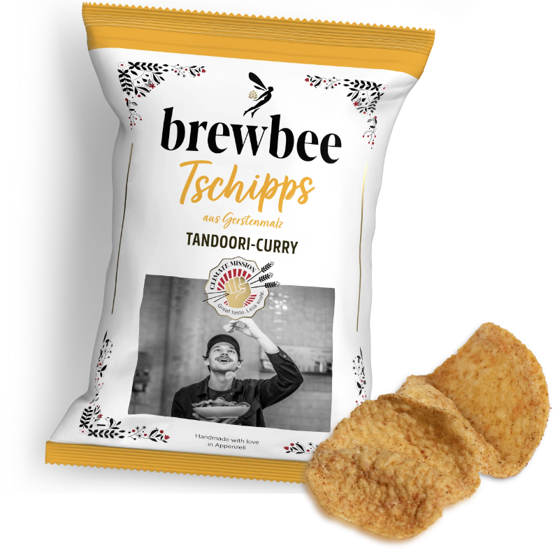 Packung brewbee Tschipps Tandoori-Curry aus Gerstenmalz mit zwei Chips davor, freigestellt vor schwarzem Hintergrund